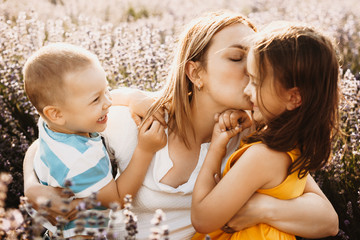 Wall Mural - lovely little girl smiling while her mother is embracing her and kissing while her brother is laughi