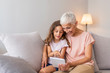 Portrait of grandmother reading stories to cute little girl using digital tablet together, copy space. Granddaughter with granny using tablet at home. Grandmother and granddaughter