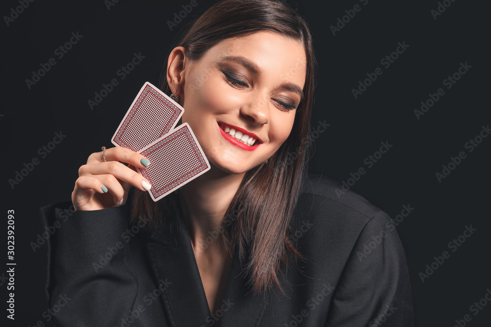 Beautiful young woman with playing cards on dark background