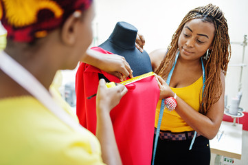 Two african dressmaker woman designed new red dress on mannequin at tailor office. Black seamstress girls.