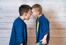 Portrait Of Two Brothers Standing Head To Head And Screaming In Studio. Boys Wearing The Same Clothes Posing Together Isolated On Wooden Background. Selective Focus.