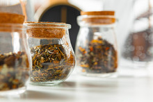 Glass Jars With Dry Tea Leaves Close Up On White Table