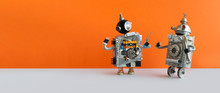 Two Mechanical Steampunk Toys On Orange Background. Funny Robot Technicians Discuss Repair Work. Copy Space