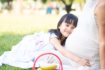 Wall Mural - Asian little daughter is hugging her mother's belly and smile with fully happiness moment in the green park, concept of love expression in family lifestyle.