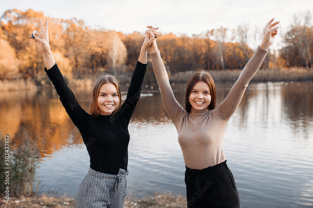 Beautiful two young twin sisters in casual outfit posing with hands up ...
