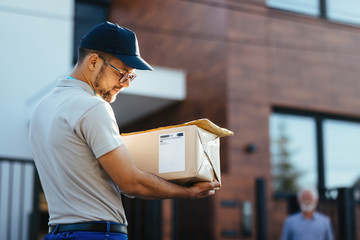 Wall Mural - Young courier reading address on package label while making home delivery.