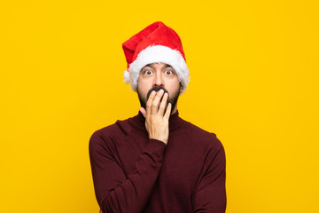 Man with christmas hat over isolated yellow background surprised and shocked while looking right