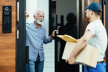 Wall Mural - Happy senior man opening door to the delivery man.