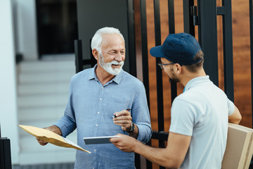 Wall Mural - Happy mature man talking to courier while signing on touchpad for a delivery.