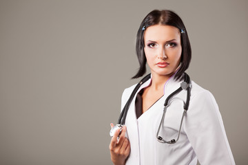 Portrait of an attractive young beautiful nurse or doctor woman with stethoscope posing on a gray background. Place for advertising. Concept of medicine and healthcare