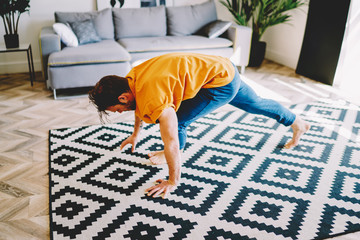 Fototapete - Young man practicing yoga poses on stylish carpet in modern apartment with home interior.Hipster guy doing morning physical exercises to maintain a healthy lifestyle and sportive shape