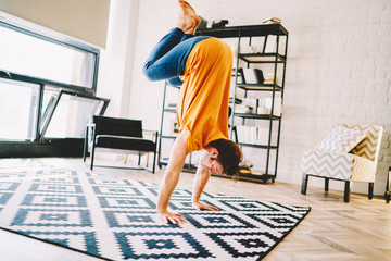 Fototapete - Experienced young man standing on hands doing yoga during morning workout on stylish carpet at home interior.Sportsman practices a healthy and energy lifestyle in modern flat