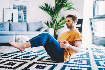 Fototapete - Young man doing yoga exercises supporting healthy lifestyle and sport body shape in home apartment with stylish interior.Hipster guy practicing meditation during morning workout in flat