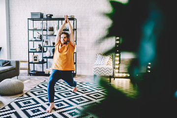 Fototapete - Motivated young bearded man holding hands in namaste above the hand during yoga training on stylish carpet in modern apartment.Hipster guy practicing meditation in poses at home