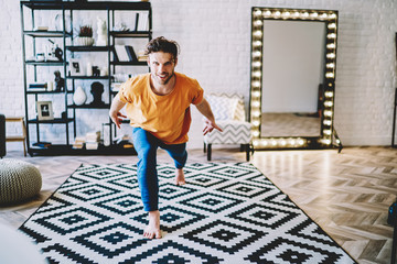 Fototapete - Portrait of positive young man smiling at camera while practicing different poses during yoga training at home interior.Motivated hipster guy warming up before meditation in modern apartment