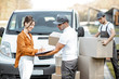 Courier delivering goods to a young woman by cargo van vehicle, client signing documents, mover with cardboard parcels on the background