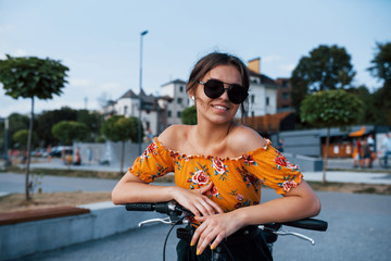 Wall Mural - Portrait of positive young girl in sunglasses that stands with her bike