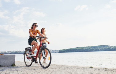 Wall Mural - Girl runs near bicycle. Two female friends on the bike have fun at beach near the lake