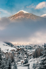 South Tyrol village in Italy during winter  with fog over city and big dolomite mountain in background / High ISO image