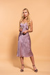 © LIGHTFIELD STUDIOS - elegant blonde woman in violet satin dress and necklace holding cocktail on beige
