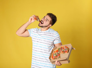 Wall Mural - Handsome man eating tasty pizza on yellow background