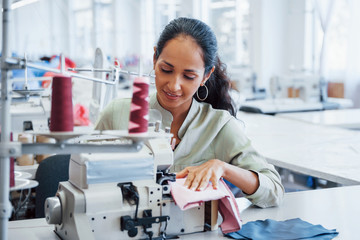 Dressmaker woman sews clothes on sewing machine in factory