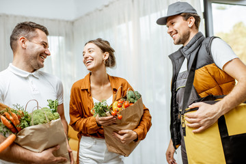 Cheerful courier in uniform delivering fresh groceries to a young family home. Online shopping and home delivery concept