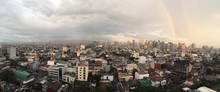 High Angle Panoramic Shot Of A Cityscape With Colorful Buildings And The Rainbow In The Cloudy Sky