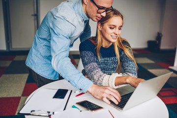 Wall Mural - Young female employee pointing on laptop computer monitor watching video with male colleague creating project,coworkers reading financial news on netbook making business plan together in office