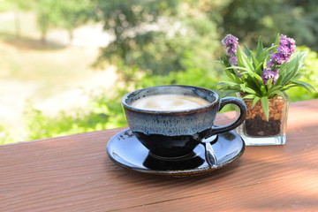 Hot coffee cup with spoon and small flowerpots put on wood table with blur background, refreshment on morning time, relaxing in the coffee shop.