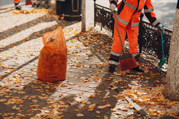 Janitor cleaner sweeping autumn leaves on the street