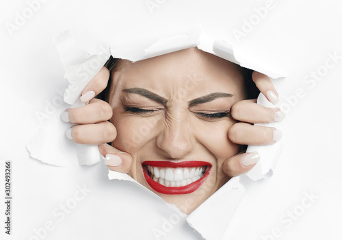 Fotografía Young beautiful woman is struggling to break through a white material wall