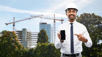 Poster - architecture, building business and people concept - smiling indian male architect in helmet showing smartphone over construction site background