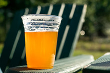 Beer In A Clear Plastic Cup, On The Armrest Of A Patio Chair