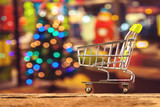 Fototapeta  - Miniature shopping cart over blurred bokeh Christmas background,for holiday shopping concept.