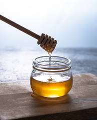 Natural vegan golden honey in a jar on wood background. The hand holds a stick, which drains the honey. Image is macro, close up and front view