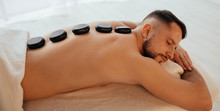 Handsome Man At Spa Resort Receive Hot Stone Massage. Speciality Massage Using Smooth, Heated Stones