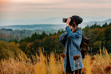 style girl with camera and backpack at countryside with mountains on background