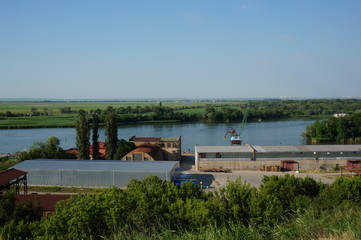 Poster - Warehouse facilities on the port territory. Port crane on the river Bank. Summer natural landscape.