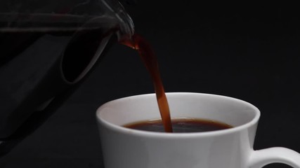 Wall Mural - close-up Person holding jug with hot black coffee and pouring into a white cup, fresh coffee, black background