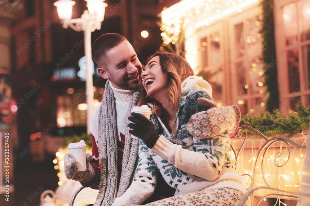 Young happy couple enjoying their romantic date while warming up with hot beverages. - obrazy, fototapety, plakaty 