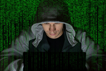 Wall Mural - The villain, a computer hacker in the hood at the computer on a background of binary code