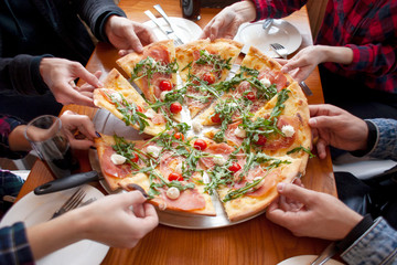 group of students friends eat Italian pizza, hands take slices of pizza in a restaurant