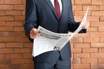 Handsome businessman with newspaper against brick wall