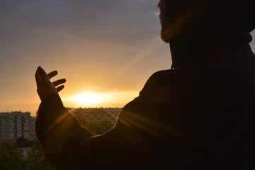 Silhouette of a hooded man preaching at sunrise