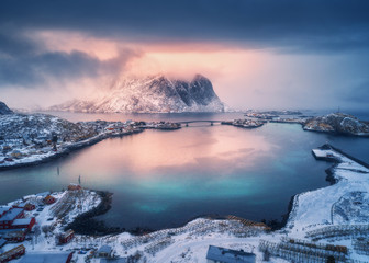 aerial view of snowy mountain, village on sea coast, orange sky at sunset in winter. top view of rei