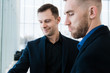 © Margo Kos - Two handsome smiling businessmen in airport, discussing important project and looking at phone screen.