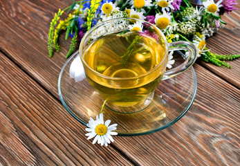 Wall Mural - Herbal tea in a glass cup with bouquet of wild flowers on a wooden background. Text space.