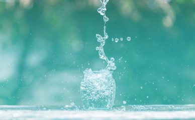 Water splash in glass Select focus blurred background.Drink water pouring in to glass over sunlight and natural green background.Nature conservation concept.