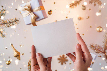 Female hands holding a letter to Santa on light golden background with flying Christmas decorations, fir branches, balls, sparkles and confetti. Xmas and New Year holiday, bokeh, light.Selective focus